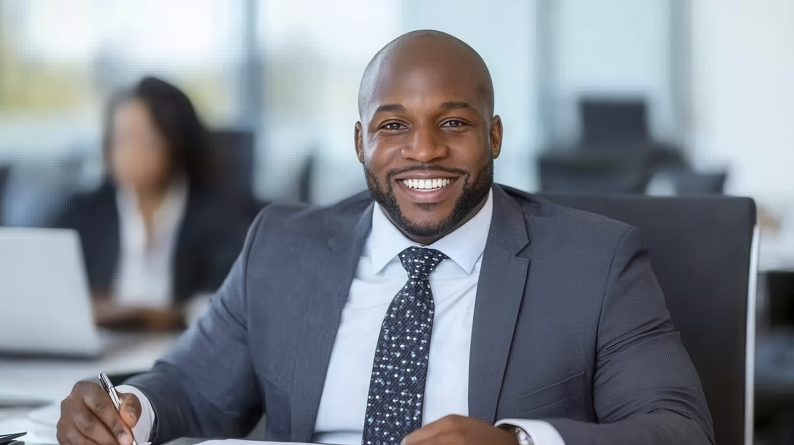 smiling businessman in gray suit writing at desk